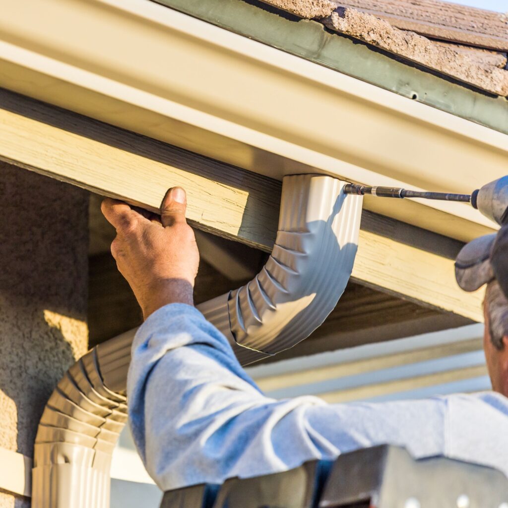 man using a drill to install or repair a gutter downspout