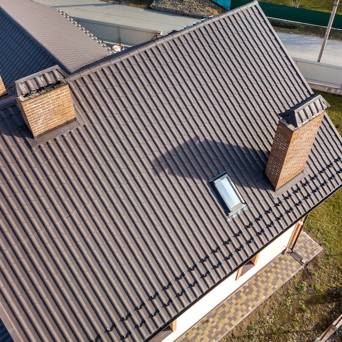 A large sloped metal residential roof with two brick chimneys with flashing around 